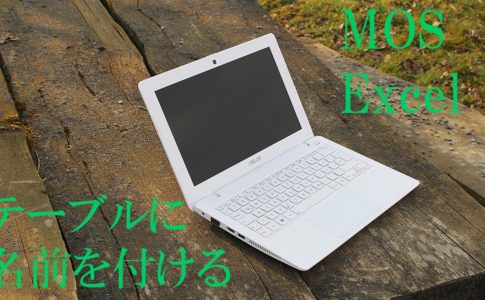 木のテーブルにパソコンが置いてある。MOS Excel　テーブルに名前を付けると書いてある